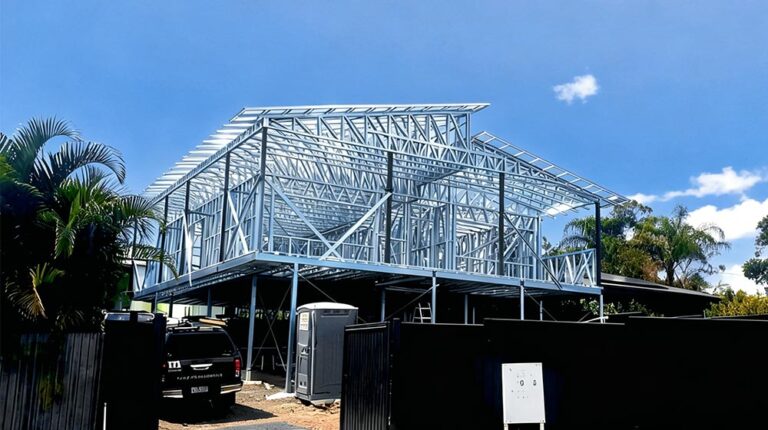 Steel house frame under construction with clear blue sky, showcasing a modern building framework with metal beams and supports.