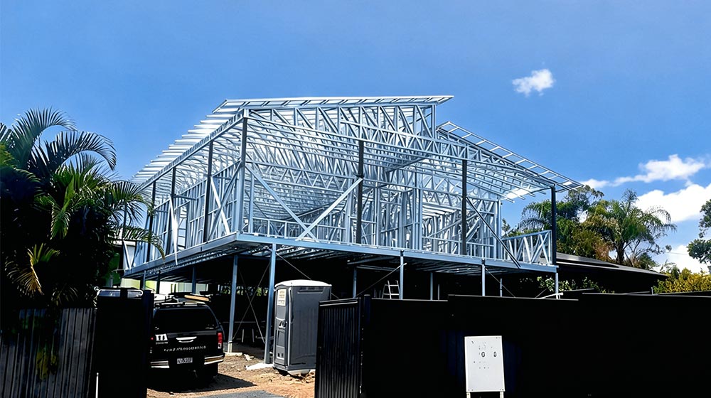 Steel house frame under construction with clear blue sky, showcasing a modern building framework with metal beams and supports.