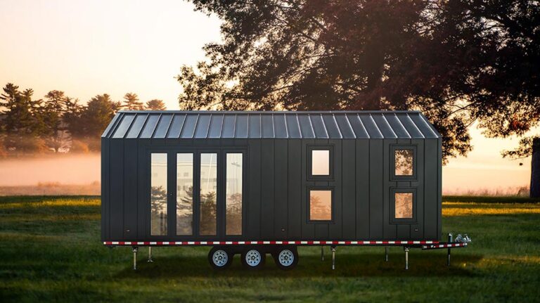 Mini-casa nera compatta su ruote dal design moderno, immersa in un tranquillo paesaggio al tramonto. Perfetta per uno stile di vita minimalista o per un rifugio mobile, progettata per durare a lungo e avere stile.