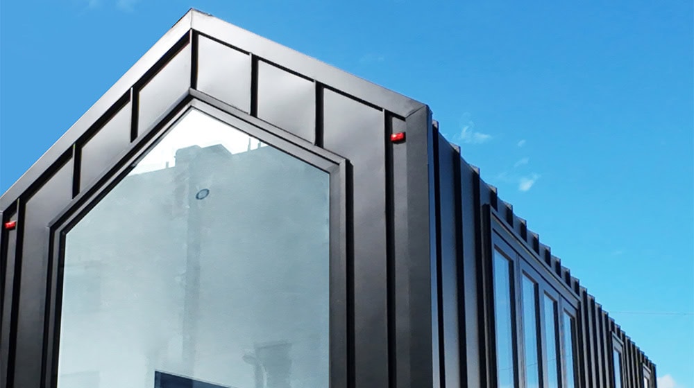Sleek modern building with black metal exterior and large glass windows under a blue sky.