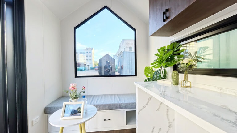 Angolo finestra moderno e minimalista con panca integrata, piano di lavoro in marmo bianco e piante decorative per un arredamento elegante.