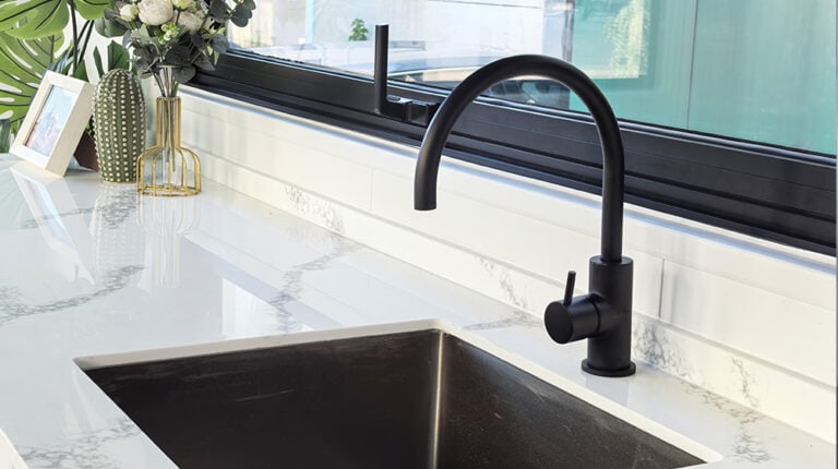 Rubinetto da cucina nero dal design moderno su un piano di lavoro in marmo bianco.