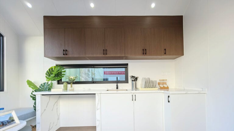 Interno di una cucina moderna con mobili bianchi, pensili in legno e piante decorative, che mette in risalto il design elegante e l'arredamento contemporaneo.