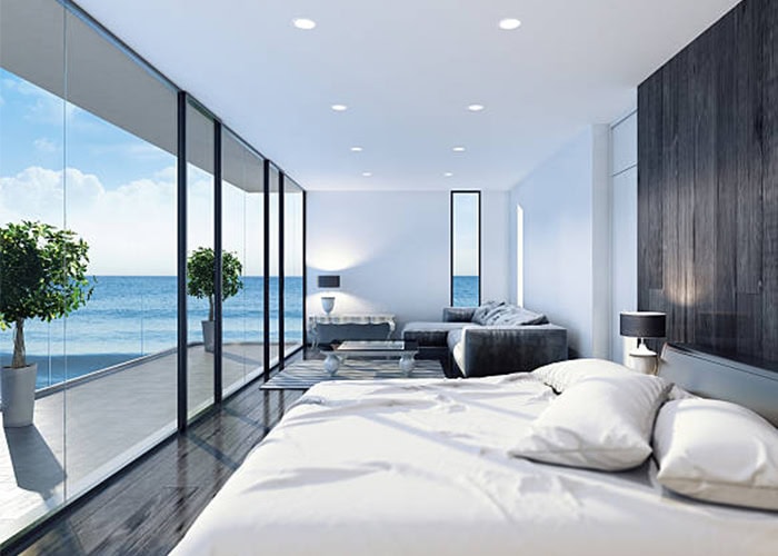 Modern oceanfront bedroom with large glass windows, contemporary furniture, and stunning sea views, showcasing luxury living and stylish interior design at Deepblue.