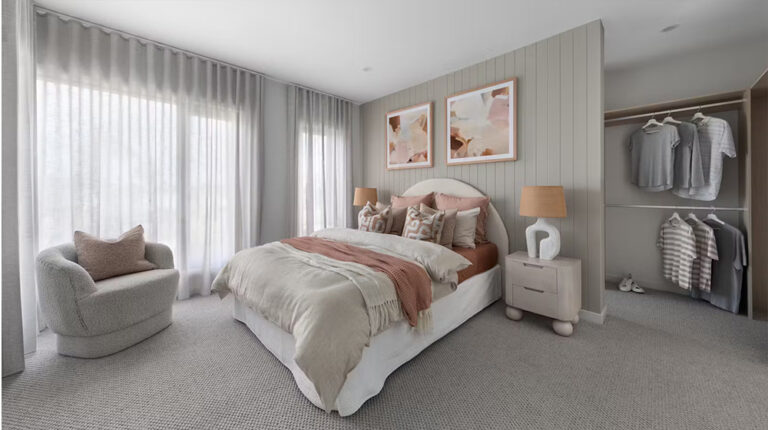 Soft neutral bedroom with elegant bedding and decor, featuring a cozy armchair, modern artwork, and an open closet with neatly arranged clothes, creating a welcoming and stylish space.