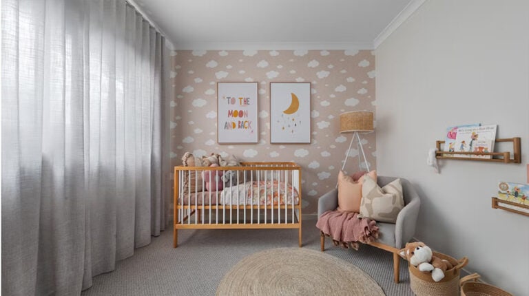 Soft nursery with cloud-themed wallpaper, children's books, cozy armchair, and wooden crib, creating a warm and calming environment for a baby or toddler.