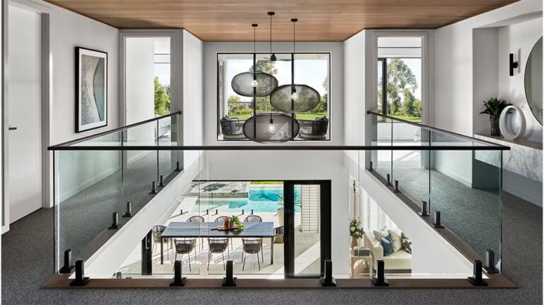 Modern two-story home interior with open loft and glass balcony overlooking dining area and outdoor pool, featuring contemporary decor and stylish lighting fixtures, perfect for luxury living.
