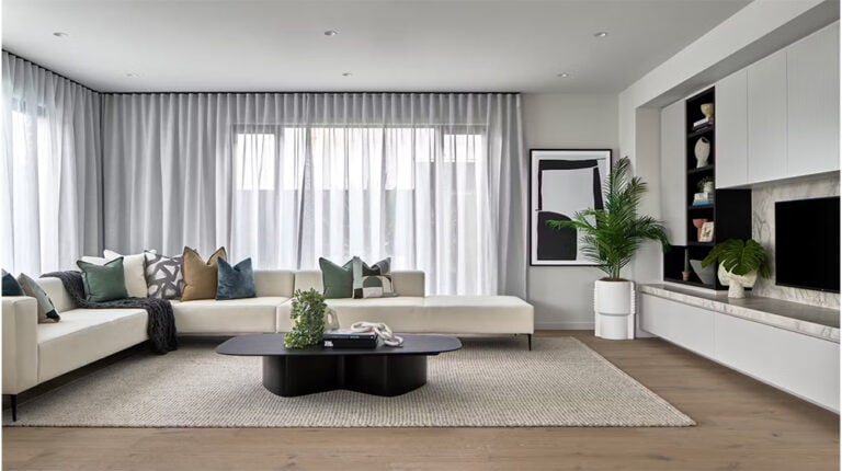 Modern living room with white sectional sofa, decorative cushions, natural light, and contemporary decor including plants and artwork, creating a stylish and inviting home interior.