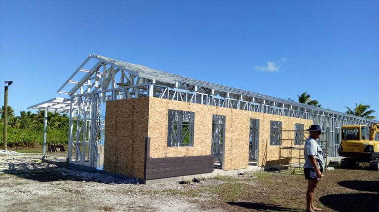 Maison à ossature métallique légère en construction, avec murs en bois, située dans une zone tropicale plantée de palmiers, illustrant des méthodes de construction écologiques pour des habitations durables.