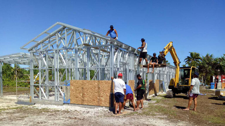 Construcción de una casa de acero en proceso con trabajadores, equipos de construcción y un entorno tropical, que muestra la experiencia en construcción de viviendas en Deepblue y soluciones de construcción innovadoras.