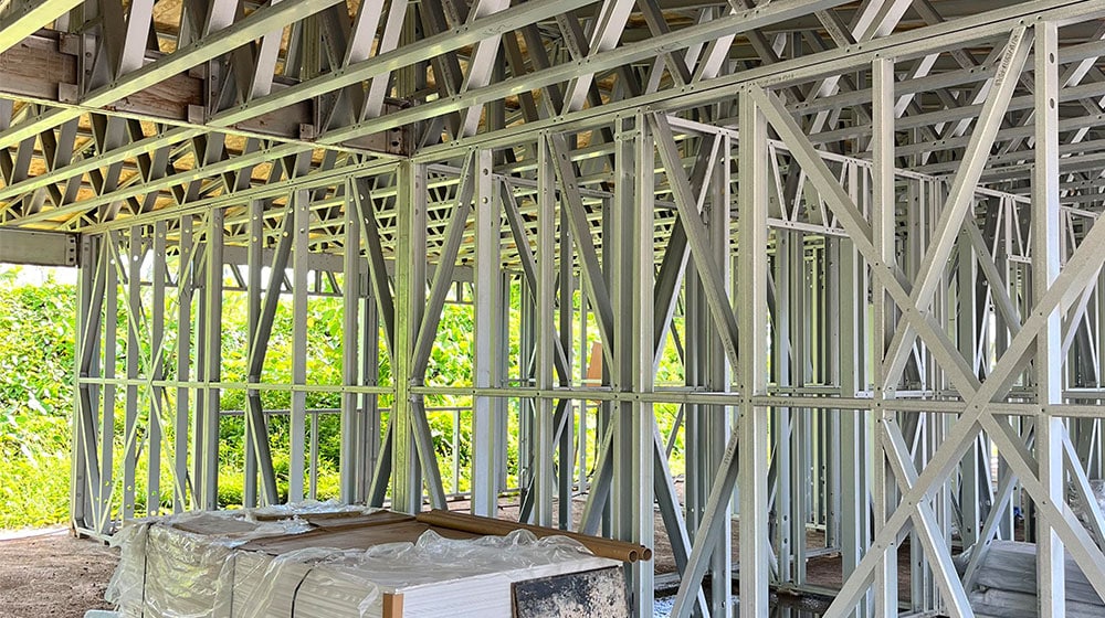 1. Metal building framework under construction with exposed trusses and studs, showcasing steel framing for residential or commercial construction projects.