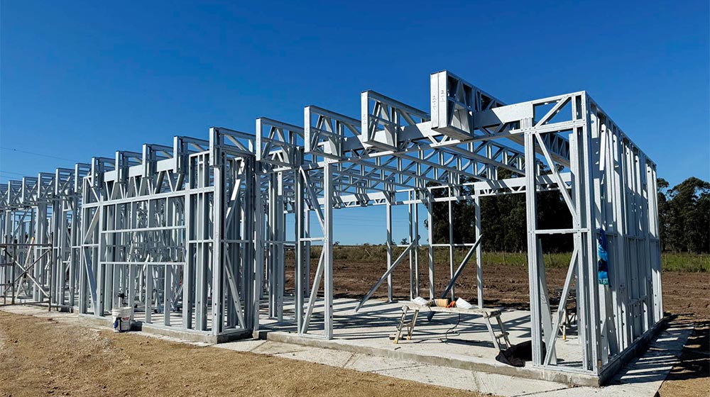 Ein im Bau befindliches Stahlrahmenhaus, dessen robuste Metallständer und -konstruktion in einer ländlichen Gegend unter strahlend blauem Himmel zu sehen sind. Ideal für nachhaltiges, individuell gestaltbares Bauen mit langlebigen, umweltfreundlichen Materialien.
