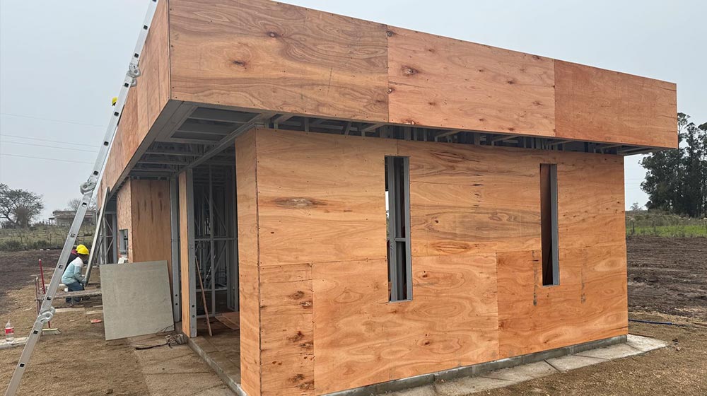 1. Wooden house under construction with plywood exterior, metal framing, and construction workers on site.