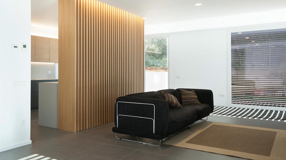 Modern minimalist living room with black sofa, wooden room divider, and large window with blinds, featuring sleek design and natural lighting for contemporary home aesthetic.