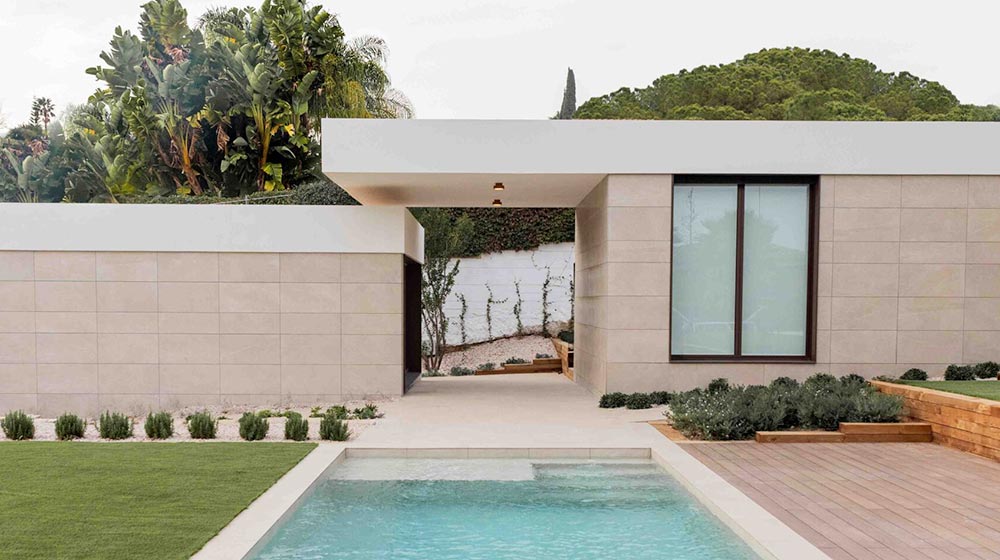 Casa moderna y minimalista con piscina privada, elegante exterior en beige, amplio ventanal, exuberante vegetación y un jardín paisajístico. Perfecta para una vida de lujo y relajación al aire libre en un entorno sereno.