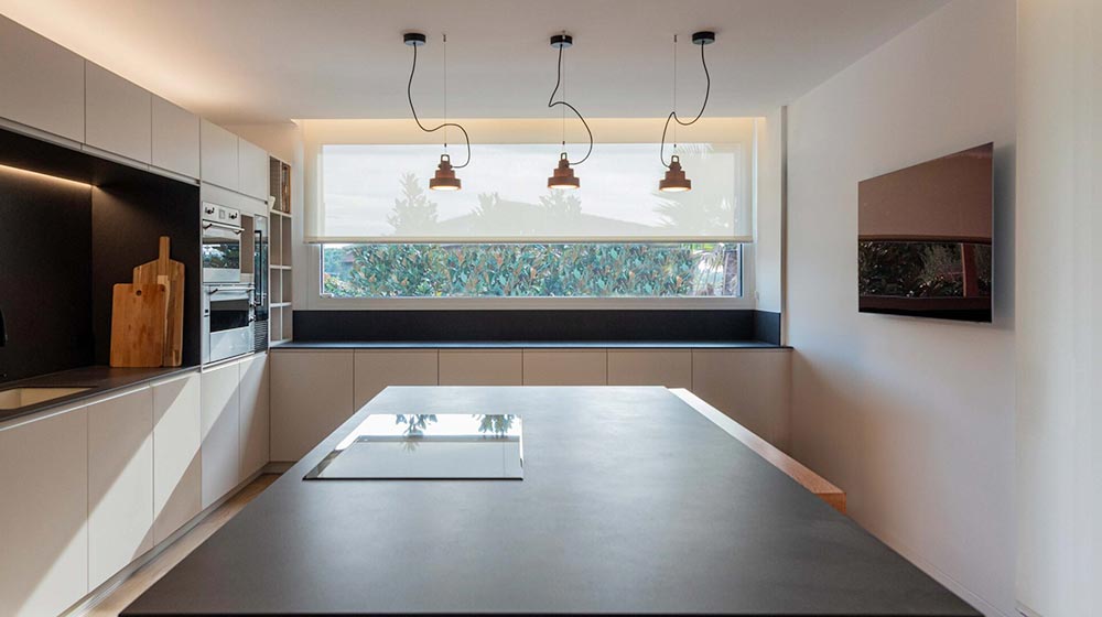 Cocina moderna contemporánea con elegantes gabinetes blancos, ventana grande con luz natural, iluminación colgante minimalista y electrodomésticos integrados, perfecta para una vida hogareña con estilo y creatividad culinaria.