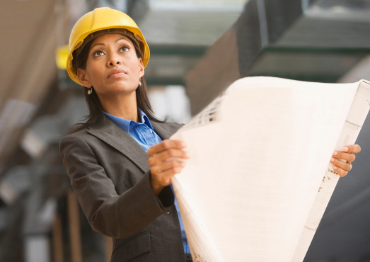A woman engineer or architect holding blueprints at a construction site, wearing a yellow safety helmet, representing engineering, architecture, and construction project planning.