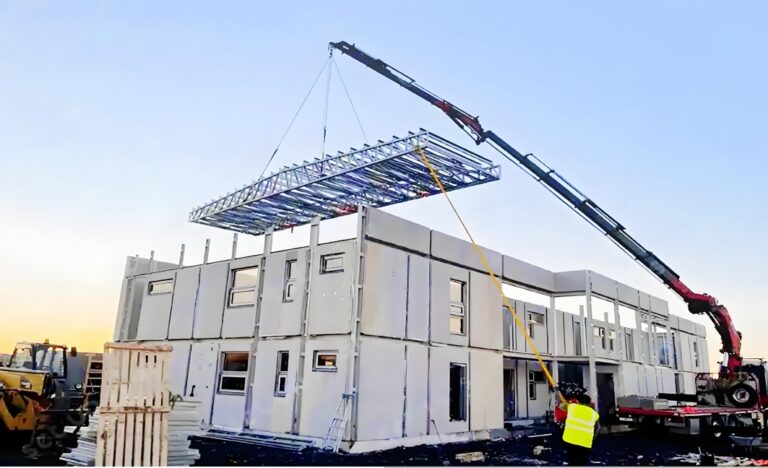 Crane lifting prefabricated building modules at construction site for modular housing.