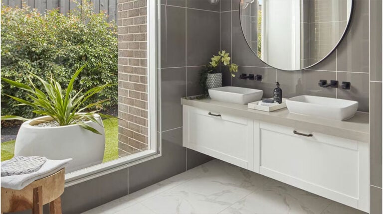 Modern bathroom with dual vessel sinks and large mirror, featuring sleek gray tiles and a view of lush outdoor greenery, combining style and functionality.