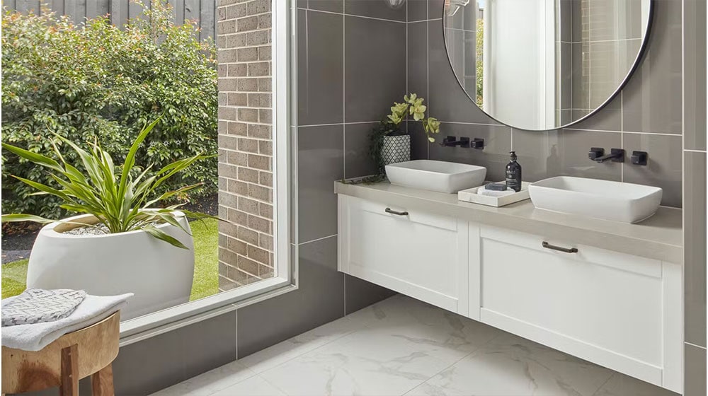 Modern bathroom with dual vessel sinks and large mirror, featuring sleek gray tiles and a view of lush outdoor greenery, combining style and functionality.