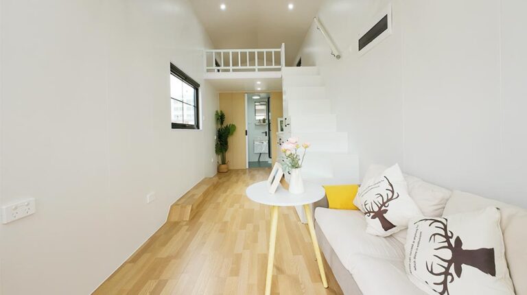 Bright minimalist living room with cozy sofa, decorative pillows, and natural wood flooring. Features a sleek staircase and open layout. Ideal for small space living with stylish decor and functional design.