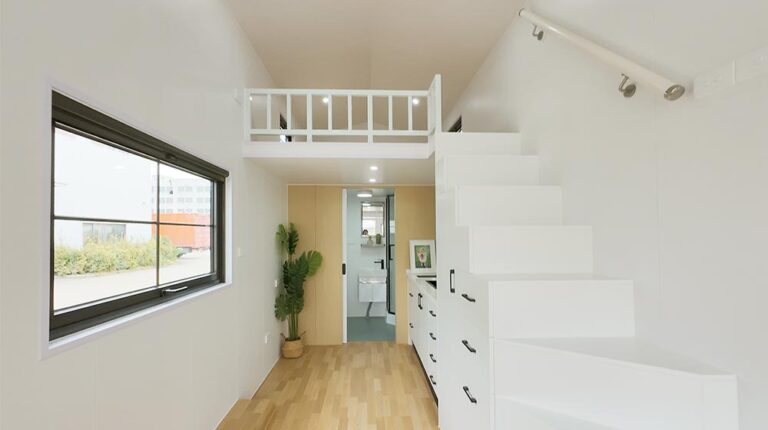 Elegant white interior of a compact tiny home space with staircase, natural light, and minimalist decor. Perfect for small, stylish living solutions, utilizing space efficiently with modern design.