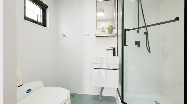 Bright minimalist bathroom featuring a compact sink, black fixtures, and a glass shower enclosure, perfect for small spaces. Clean white walls and sleek design enhance bathroom functionality and style.