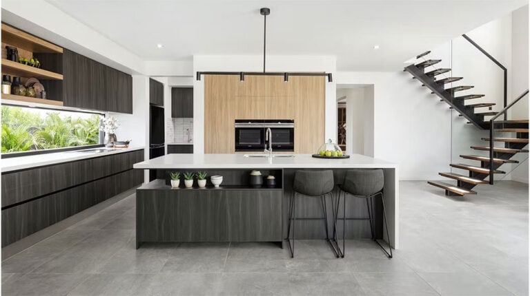 A sleek, contemporary kitchen featuring a central island with seating, wooden cabinetry, minimalist decor, and a staircase leading to the upper level, perfect for modern home living.