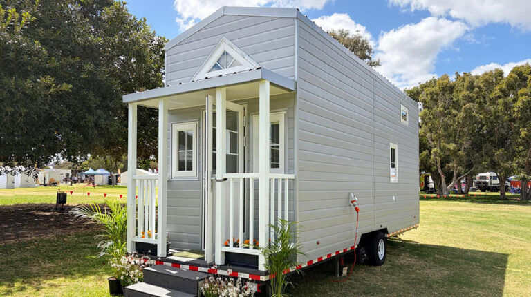 Portable tiny home with grey siding, small porch, and eco-friendly design, perfect for outdoor living or events. Features include energy-efficient windows and mobile setup.