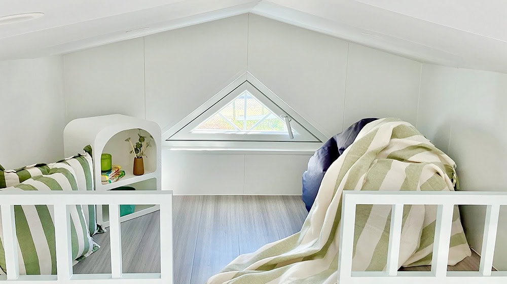 Bright attic bedroom featuring minimalist design with cozy bedding and a triangular window for natural lighting.