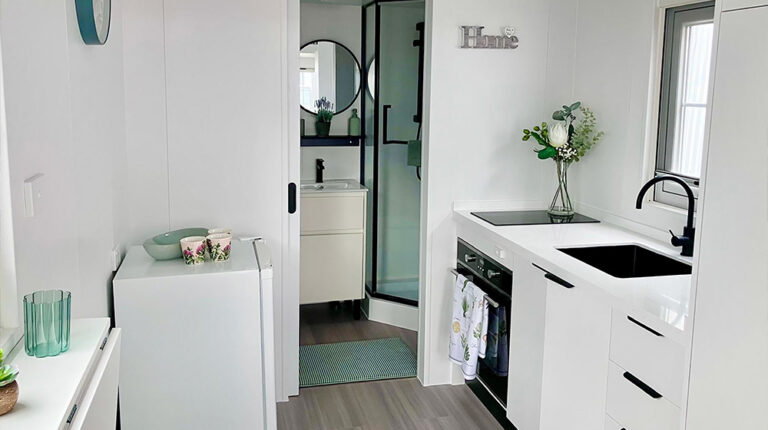 Bright, sleek white kitchen with modern sink, black faucet, and ample storage, perfect for contemporary living spaces. Features a stylish glass door shower and decorative interior plants for a fresh, homey feel.