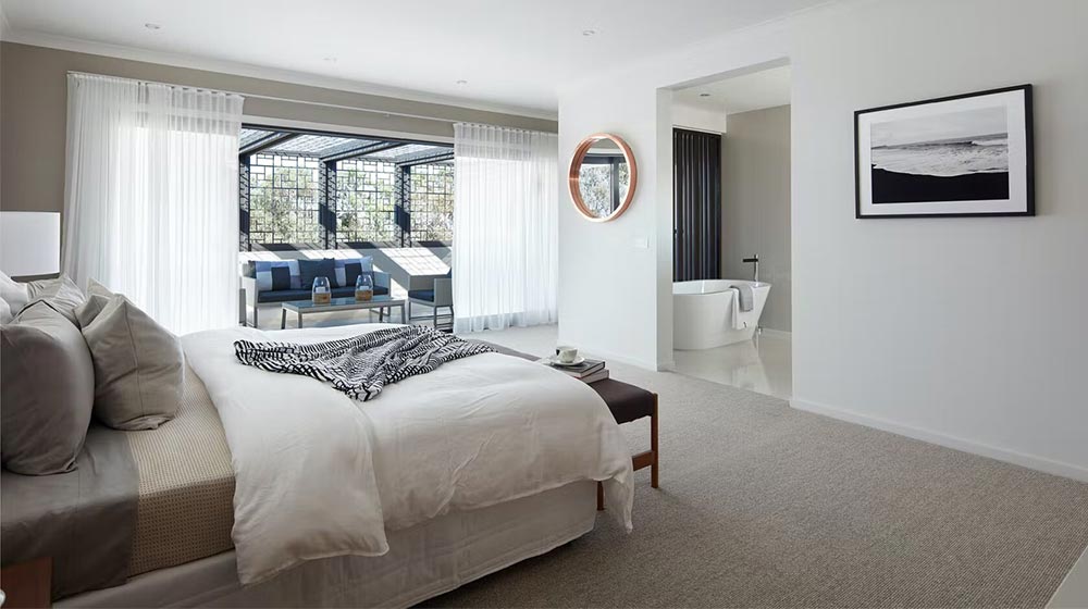 Bright bedroom with ocean view and modern decor, featuring a white bed, natural light, and a cozy seating area, perfect for relaxation and comfort.