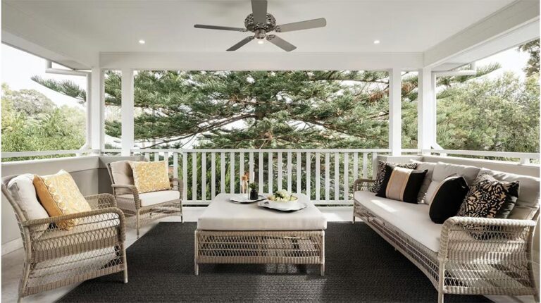 Elegante patio esterno con divani in rattan, cuscini e un tavolino da caffè con vista sugli alberi.