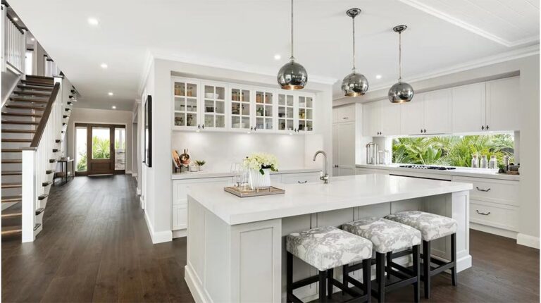 Cucina bianca e luminosa con luce naturale, mobili eleganti e lampade a sospensione raffinate, perfetta per uno stile di vita contemporaneo.