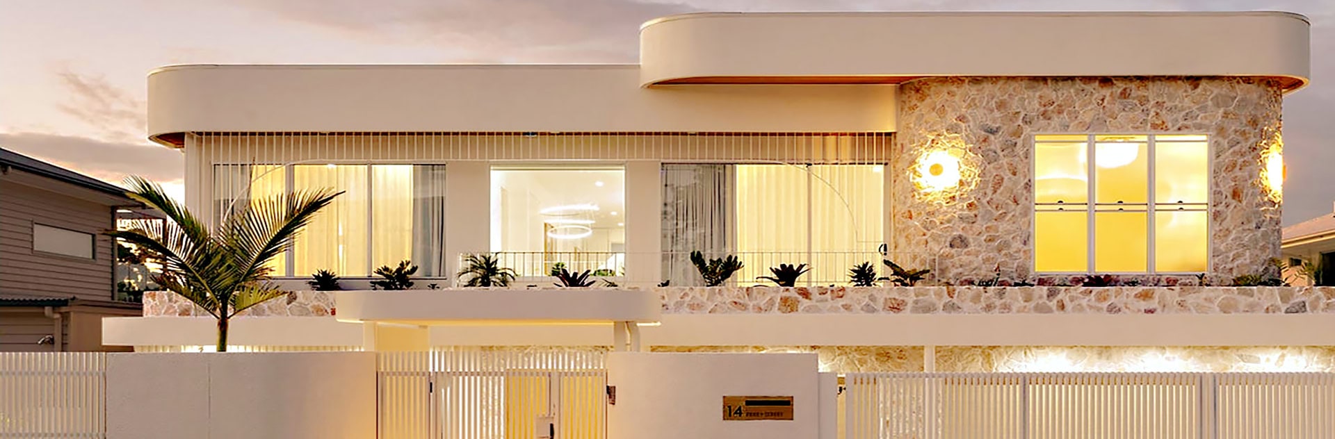 Luxury modern house with elegant architecture, large windows, and tropical plants in the front yard.