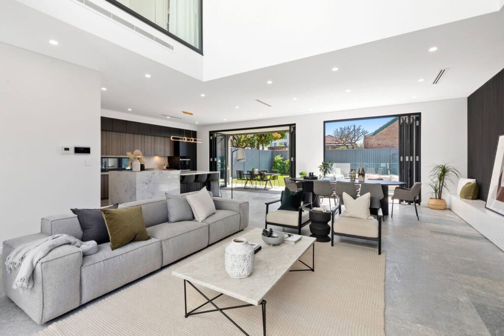 Bright open-concept living room featuring large sliding glass doors that open to a lush garden, with contemporary furniture, neutral tones, and abundant natural light.
