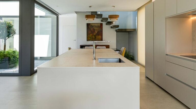 Modern minimalist kitchen featuring a spacious island, contemporary cabinetry, and large windows that bring in natural light, creating an elegant and functional space.