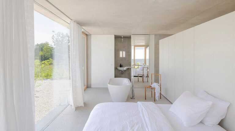 Bright and airy bedroom in a Champagne House, featuring minimalist design, large windows with views of greenery, white bedding, and elegant decor for a luxurious stay.
