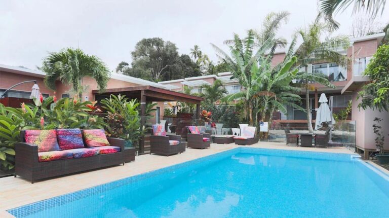 Relaxing tropical poolside lounge with lush greenery, outdoor seating, and a modern design, showcasing the benefits of prefab wooden structures in the Cook Islands Bungalow Project.