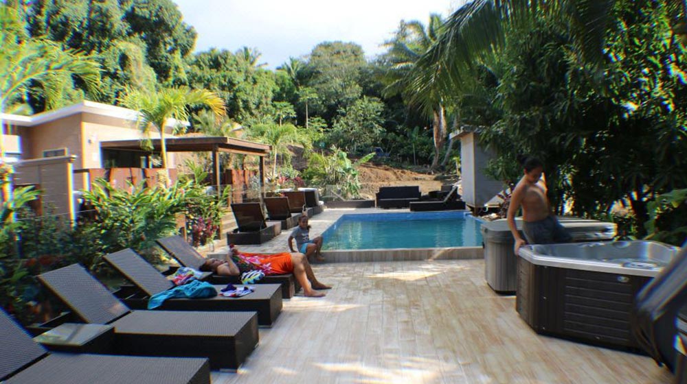 Moderno bungalow prefabbricato in legno nelle Isole Cook con piscina esterna, zona relax e lussureggiante giardino tropicale, che esemplifica la costruzione sostenibile e il comfort della vita isolana.