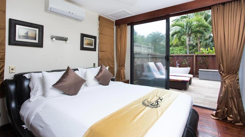 Elegant wooden bungalow interior with large glass doors and tropical outdoor view.