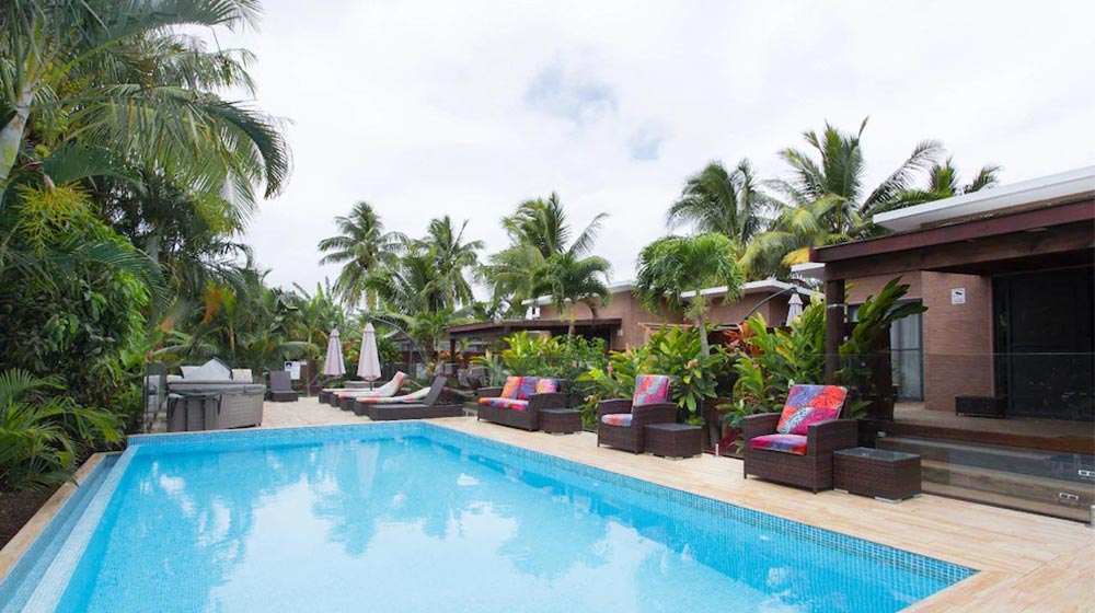 Outdoor pool with tropical lounge chairs and lush greenery in Cook Islands bungalow resort. Perfect for relaxation and enjoying island paradise views.