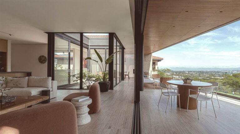 Modern minimalist steel home interior featuring large glass doors, spacious living area, and a balcony with scenic views, ideal for contemporary sustainable living.