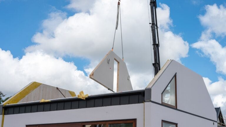 Crane lifting prefabricated wall panel onto modern modular house under construction