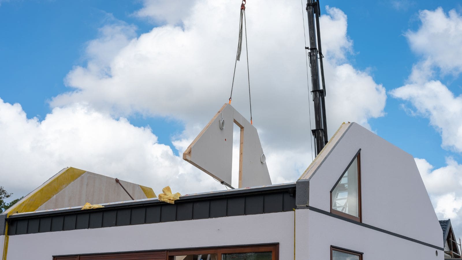 Crane lifting prefabricated wall panel onto modern modular house under construction