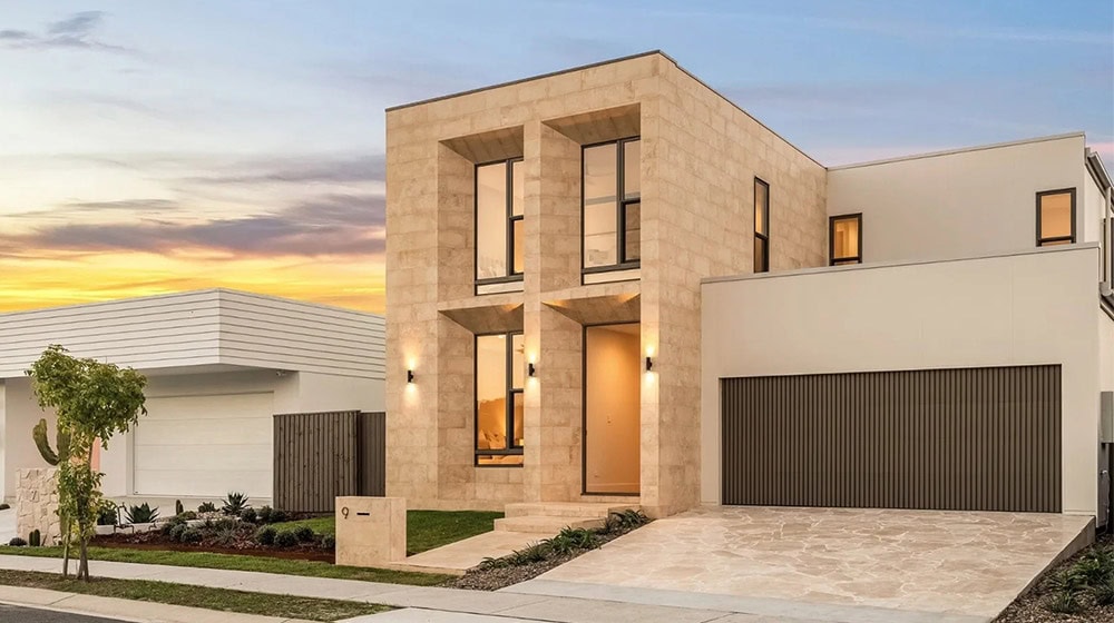Contemporary residential house with clean lines and modern design, featuring large windows and a spacious driveway, set against a sunset sky.