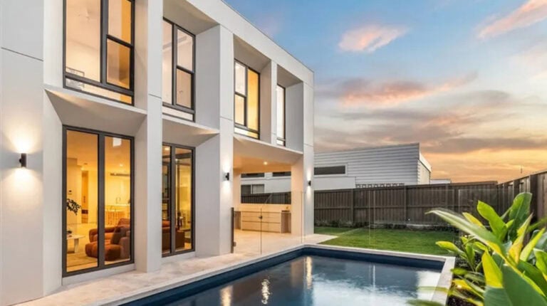 Contemporary house with large glass windows and a swimming pool, illuminated by sunset light, in a residential area of Gold Coast.