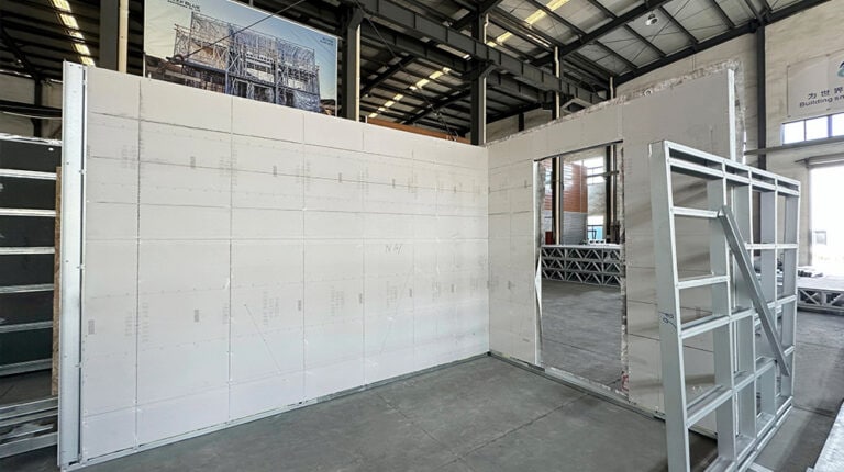 Interior view of a construction site showing a white wall with a window opening and construction materials in an industrial setting.