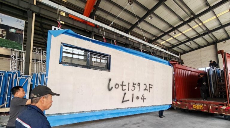 Large prefabricated modular unit being transported inside a factory, with workers observing, showcasing advanced construction technology by Deepblue.