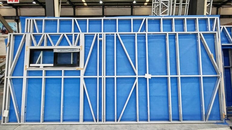 Structural frame of a panelized building system with blue weather-resistant sheathing and window opening, used in modern home construction.